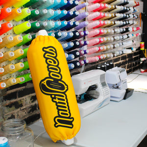 Yellow gold NautiCovers Premium Boat Fender Cover sitting on sewing table with wall of colorful threads